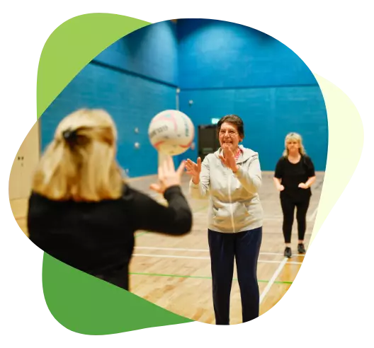 Older women playing a game of netball in an indoor sports hall, staying active and engaged.