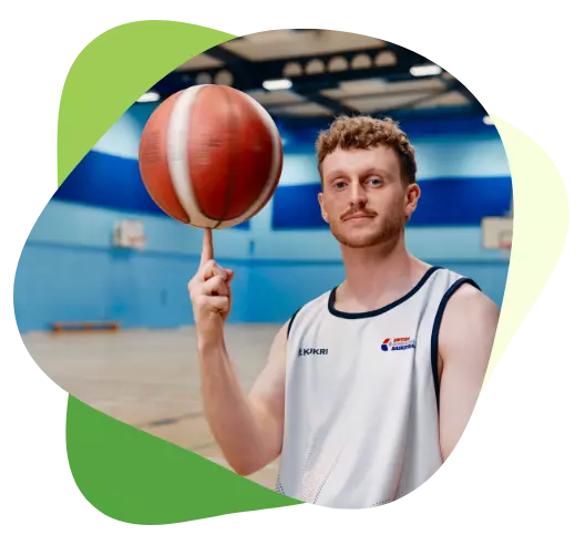 Young man in sports kit spinning a basketball on his finger in an indoor sports hall.
