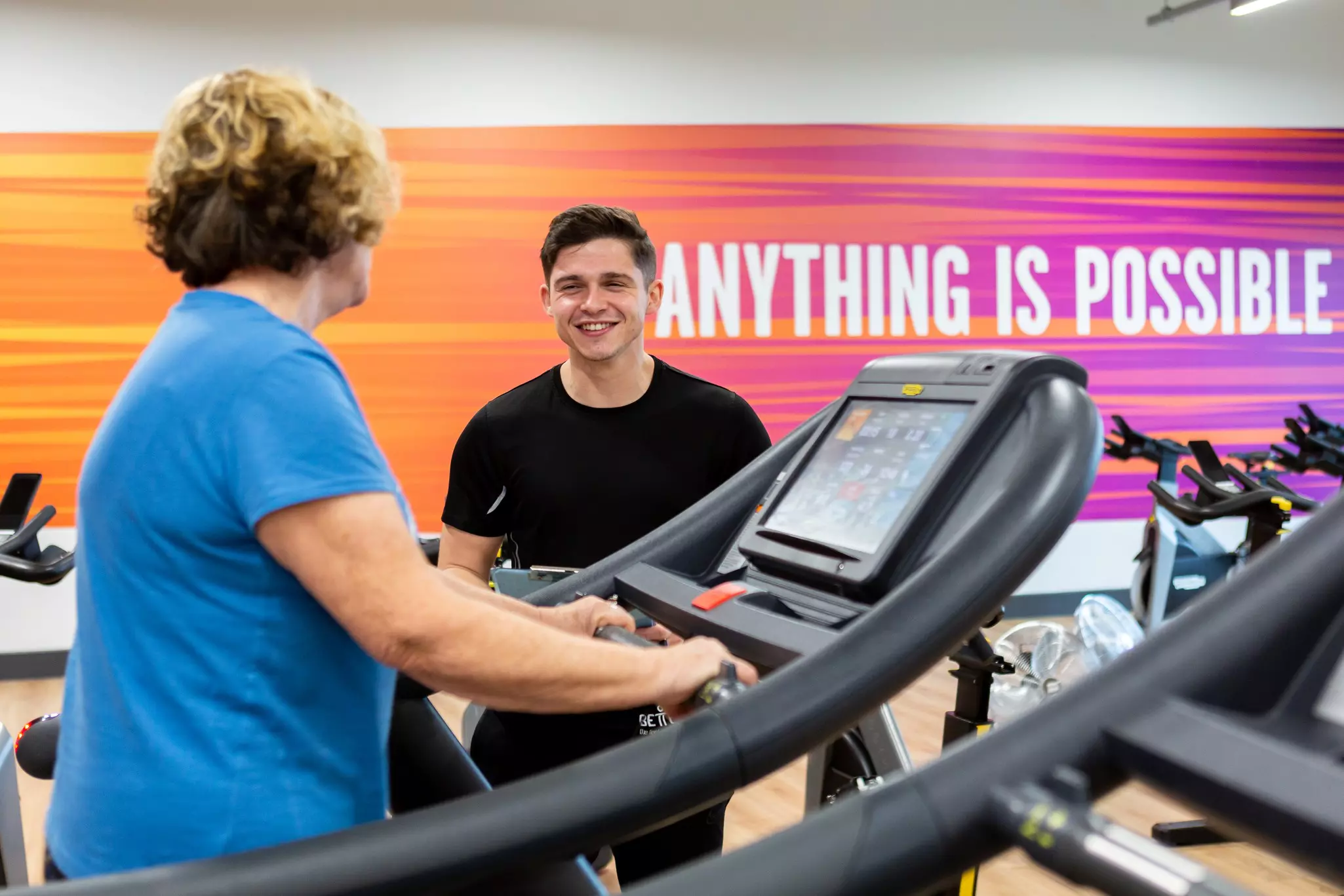 Woman on a treadmill chatting to staff member.