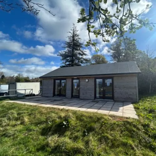 Modern wooden lodge with large windows set on a grassy area..