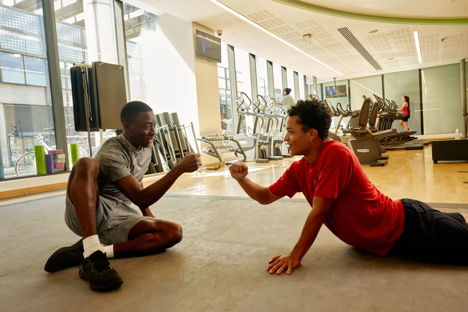 Two boys doing a fist bump while sitting on a gym floor.