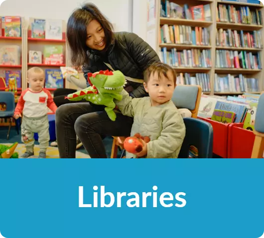 Mother and young children enjoying playtime with books and toys in a colourful library.