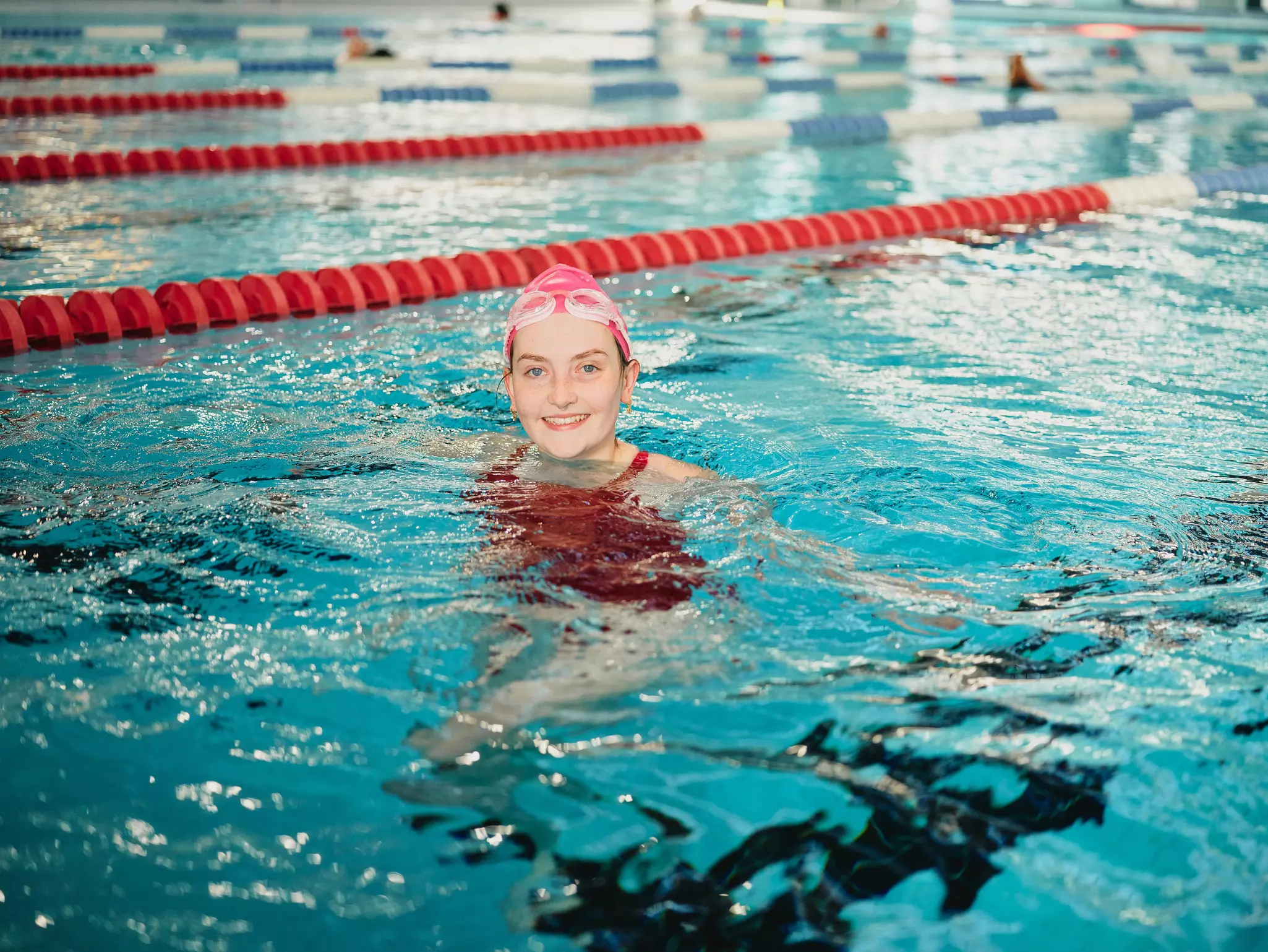 Person swimming in pool lane with red divider and other swimmers.